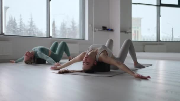Zwei schlanke junge Frauen führen auf würfelförmigen Podesten liegend Rückenübungen aus. Dehnung und Spannkraft der Rückenmuskulatur. Verbesserung der Haltung — Stockvideo