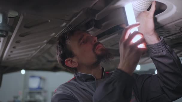 Man auto mekaniker ser under bilen upp på hissen på jakt efter fel i slow motion — Stockvideo