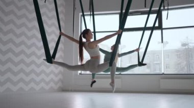 Havadaki hamaklarda iki kadın sicim yapıyor. Havada spor salonunda esneme izleri var. Aero Yoga