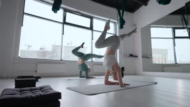 Two women standing in their arms perform twine upside down. Stretching training together in the gym. Pilates and Stretch trainer and student — Stock Video