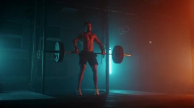 Modern fitness merkezinde kaslı fitness adamı halterle kafasına vuruyor. İşlevsel eğitim. Kapma egzersizi. Yavaş çekim rengi LED ışık, doymuş parlak renkler