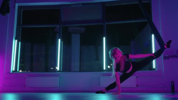 Una donna fa yoga e si estende su un'amaca appesa in luce al neon. Giovane ragazza del corpo abbastanza sottile fitness praticando fly yoga in palestra. — Video Stock