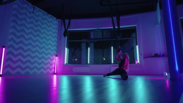 Žena dělá jógu a natahuje se na visící houpací síť v neonovém světle. Mladý pěkný štíhlý tělo fitness dívka cvičení létat jóga v tělocvičně. — Stock video