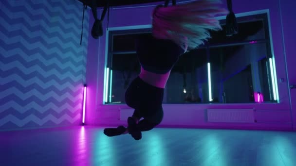 一个女人在霓虹灯下做瑜伽和伸展吊床。一个女人在工作室的吊床上做伸展运动和身体锻炼。在空气中练习 — 图库视频影像