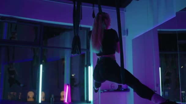 Eine Frau macht Sport-Yoga in der Luft auf einer Hängematte in Neonlicht und führt anmutige Übungen und Bewegungen aus Dehnen und Tanzen in Zeitlupe aus. — Stockvideo
