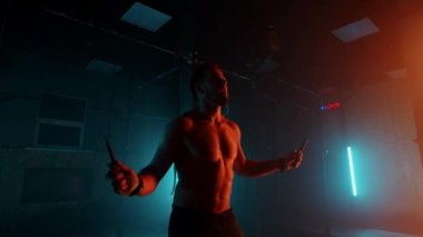 Ağır çekimde ip atlayan bir adam. Vücut geliştiren adam karanlık ve modern bir haçla ipin üstüne atlıyor.