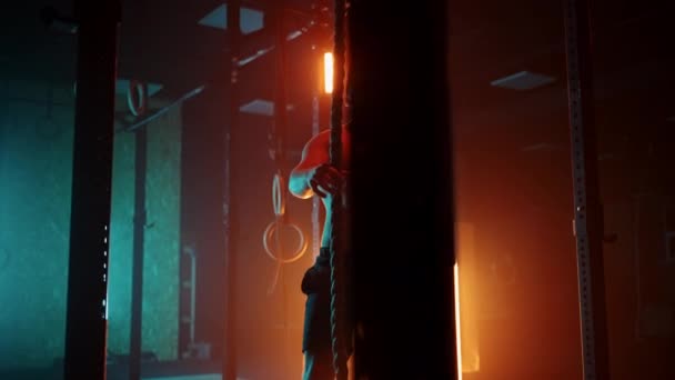 Fitness man doet touw klimmen oefening in de sportschool slow motion. Oranje blauw neon licht. Man aan het trainen in een fitnessruimte — Stockvideo