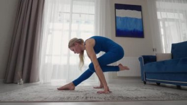 Evde bir kadın evden çıkmadan yoga egzersizleri yapıyor. Evde eğitim. Mavi takım elbiseli bir kadın halıda antrenman yapıyor.