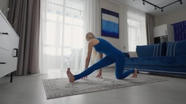 Karantinada evde kalan ve evden uzaktan çalışan bir kadın, halının üzerinde dururken antrenman yapıyor ve dengeyi sağlıyor. Spor kıyafetleri spor yapıyor, yağ yakıyor, kalori çalıştırıyor.