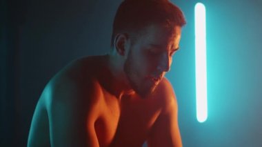 Yorgun bir sporcu ağır çekimde egzersiz yaptıktan sonra neon ışıklı bir halterde otururken ağır ağır nefes alıyor. İyileş ve yeni bir atılım için hazırlan.