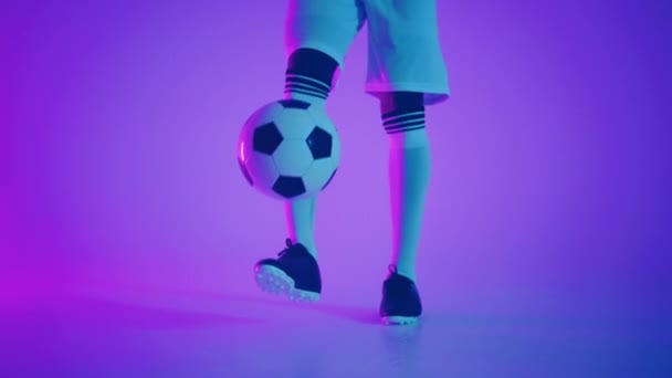 黒人選手は暗いスタジオでサッカーボールをジャグリングし、床にネオンライト、スローモーションで赤と青の照明効果があります。アフリカのプロサッカー選手 — ストック動画