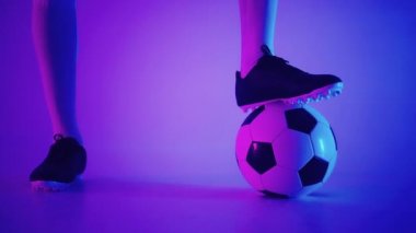 Stüdyonun mavi-kırmızı neon ışığı altında ağır çekimde topun üzerinde duran profesyonel bir siyahi futbolcunun ayağına yakın çekim. Brezilyalı futbolcu poz vermek için topa bastı