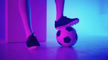 Stüdyonun mavi-kırmızı neon ışığı altında ağır çekimde topun üzerinde duran profesyonel bir siyahi futbolcunun ayağına yakın çekim. Brezilyalı futbolcu poz vermek için topa bastı