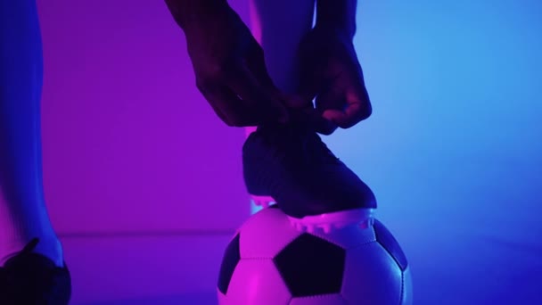 Primer plano del jugador de fútbol negro africano atando cordones en el estudio, cámara lenta. El futbolista se ata el zapato. Sección baja. atar botas de fútbol preparándose para un partido de fútbol — Vídeos de Stock