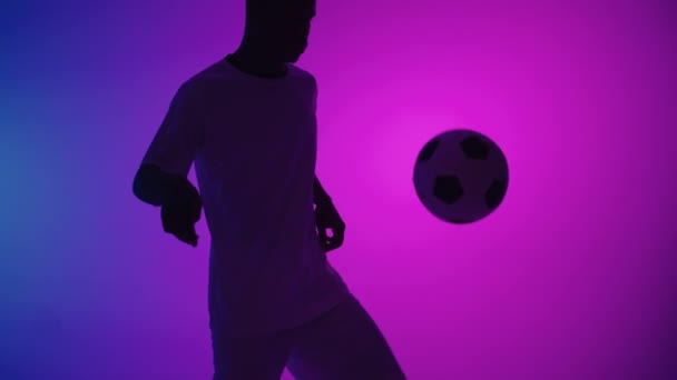 Svart man en spelare jonglerar fotboll i en mörk studio med neonljus på golvet och röda och blå ljuseffekter i slow motion. Afrikansk professionell fotbollsspelare — Stockvideo