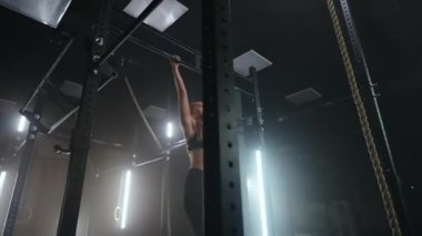 Sportif genç bir kadın karanlık bir spor salonunda, güzel bir neon arka ışıkta kendini yatay bir çubuğa çekiyor. Hedefe doğru hareket etmede dayanıklılık ve azim