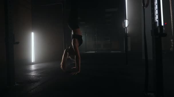 A strong young athletic woman goes upside down on her hands in the gym. A woman is fit on her hands in a dark gym. Training at least upside down — Stock Video