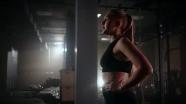 Genç bir kadın antrenmandan sonra dinleniyor ve aşağıya bakıyor. Kadın sporcu, spor salonunda spor yaptıktan sonra dinleniyor.