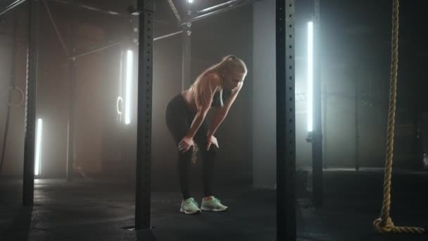 Junge Frau ruht sich nach dem Training aus und schaut nach unten. Sportlerin ruht sich nach Fitnesstraining in dunkler Turnhalle aus — Stockvideo