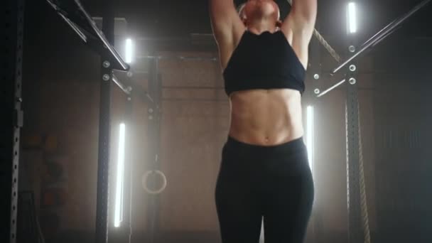 A sporty young woman pulls herself up on a horizontal bar in a dark gym in a beautiful neon backlight. Endurance and perseverance in pulling up movement towards the goal — Stock Video