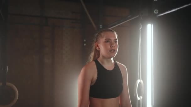 Young woman resting after her workout and looking down. Female athlete taking rest after fitness training in dark gym — Stock Video