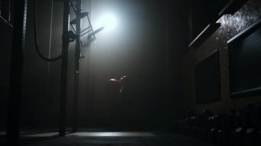 Spor salonunda çömelmiş bir şekilde top atan bir kadın. Kafasına top atan bir kadının silueti. Topla çömelmiş.