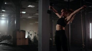 Ağır çekimde, bir kadın karanlık bir spor salonunda çalışırken kafasının üzerine bir dambıl kaldırır. Atletik güçlü kadın halterleri kaldırarak zor bir egzersiz yapıyor.