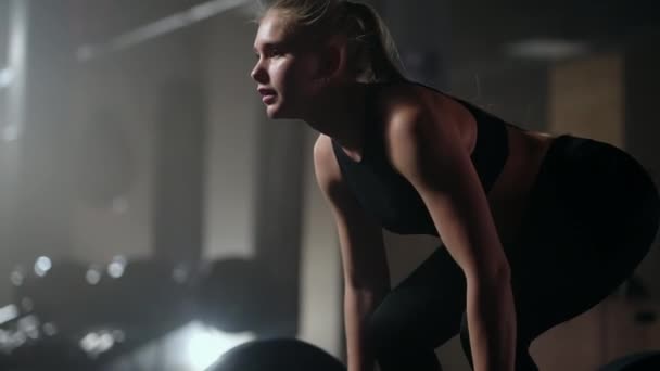 Slow motion: Een vrouw tilt een lange halter in een donkere sportschool met veel gewicht. Een sterke jonge vrouw tilt gewichten voor een training — Stockvideo