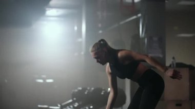 Ağır çekimde, bir kadın karanlık bir spor salonunda çalışırken kafasının üzerine bir dambıl kaldırır. Atletik güçlü kadın halterleri kaldırarak zor bir egzersiz yapıyor.