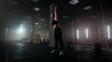 Ağır çekimde, bir kadın karanlık bir spor salonunda çalışırken kafasının üzerine bir dambıl kaldırır. Atletik güçlü kadın halterleri kaldırarak zor bir egzersiz yapıyor.