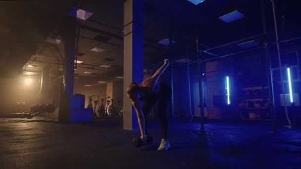 I slowmotion løfter en kvinde en håndvægt over hovedet, mens hun træner i et mørkt motionscenter. Atletisk stærk kvinde udfører en vanskelig træning med løft af håndvægte – Stock-video