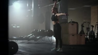 Ağır çekimde, bir kadın karanlık bir spor salonunda çalışırken kafasının üzerine bir dambıl kaldırır. Atletik güçlü kadın halterleri kaldırarak zor bir egzersiz yapıyor.