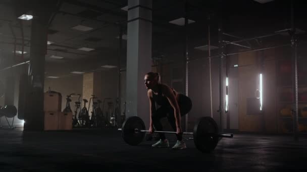 Movimento lento: Uma mulher levanta um sino em um ginásio escuro com muito peso. Uma jovem forte levanta pesos para um treino — Vídeo de Stock