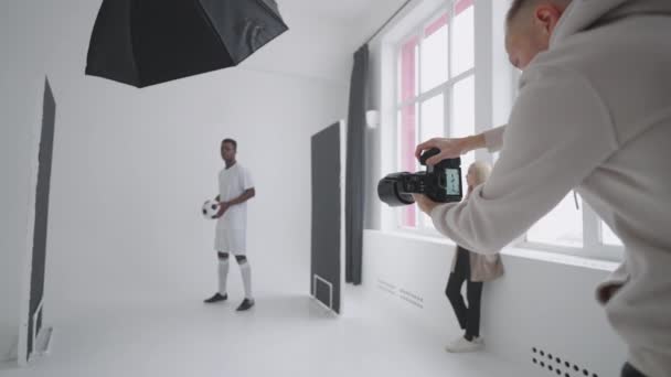 En sportsmodell av en svart mann poserer for reklameplakater. Han spiller med ballen for spektakulære skudd. Stilish Fashionable Sports Magazine (engelsk). Fotografering med profesjonelt utstyr i studioet – stockvideo