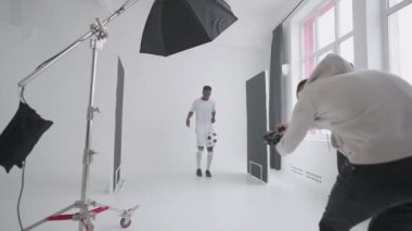 Sanat yönetmeni fotoğrafları monitörden kontrol ediyor. Profesyonel ekip stüdyoda bir arada. Profesyonel futbolcu ve prodüksiyon sahnesinin arkasında büyük bir stüdyo var..