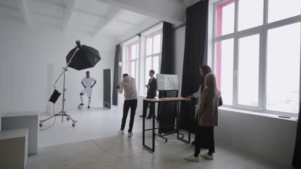 Ένα σπορ μαύρο ανδρικό μοντέλο ποζάρει για διαφημιστικές αφίσες. Παίζει με την μπάλα για θεαματικές βολές. Κομψό περιοδικό σπορ μόδας. Φωτογράφηση με επαγγελματικό εξοπλισμό στο στούντιο — Αρχείο Βίντεο