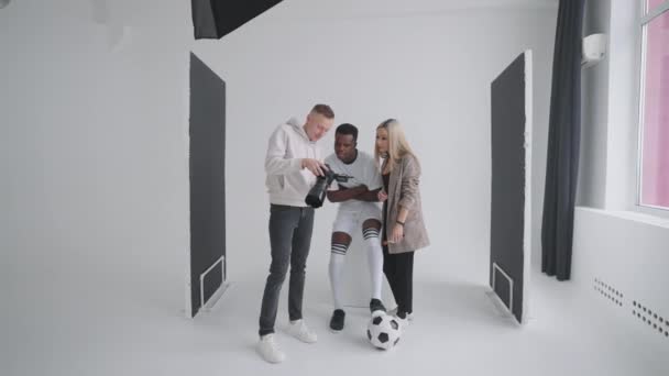 Ένας φωτογράφος, ένας ποδοσφαιριστής, ένα μοντέλο και ένας σκηνοθέτης κοιτούν φωτογραφίες από μια φωτογράφηση για το εξώφυλλο ενός διαφημιστικού περιοδικού σε μια κάμερα — Αρχείο Βίντεο