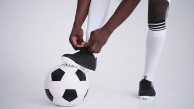 Stüdyoda ayakkabı bağcığı bağlayan siyah Afrikalı erkek futbolcuları yakın çekim, yavaş çekim. Futbolcu ayakkabısını bağlıyor. Alçak kesim. Beyaz arka planda hazırlanan futbol botları bağlanıyor