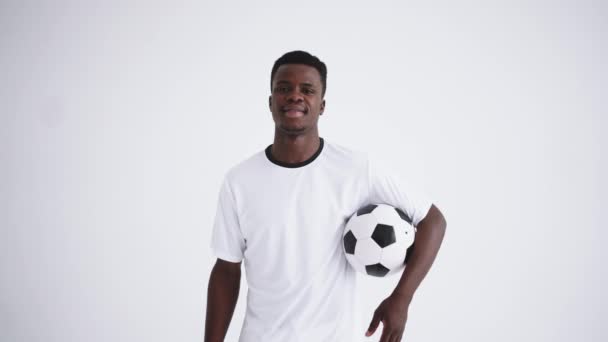 Retrato de un jugador de fútbol feliz de un grupo étnico africano con un uniforme blanco sobre un fondo blanco con una pelota en sus manos — Vídeos de Stock