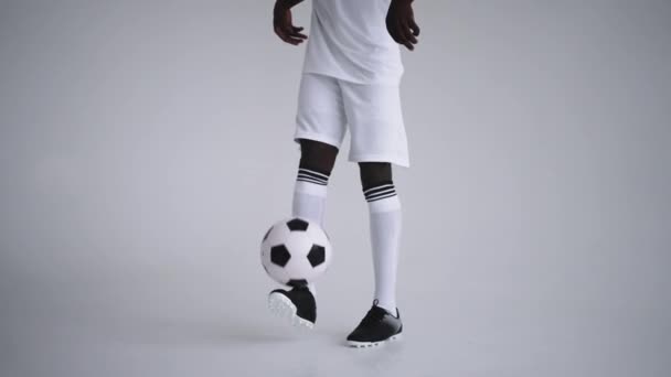 A professional black football player in a white uniform on a white background juggles a ball in slow motion. African-American ethnic group soccer player with a soccer ball — Stock Video