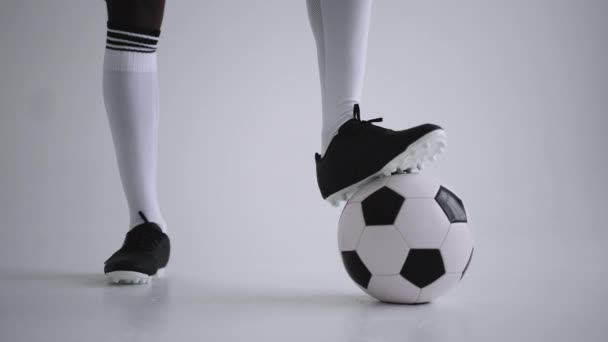 Gros plan du pied d'un footballeur noir professionnel debout sur le ballon au ralenti en arrière-plan blanc. Joueur de football brésilien pied sur le ballon pour poser — Video