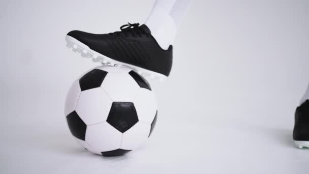 Gros plan du pied d'un footballeur noir professionnel debout sur le ballon au ralenti en arrière-plan blanc. Joueur de football brésilien pied sur le ballon pour poser — Video