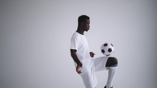 Movimiento lento: un jugador de fútbol africano camiseta blanca haciendo malabares en silueta sobre fondo blanco. Un jugador de fútbol brasileño negro hombre silueta — Vídeos de Stock