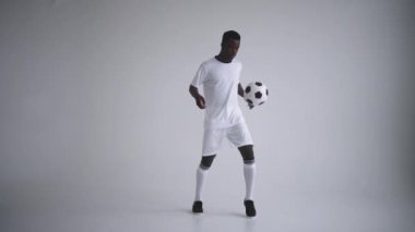 Beyaz arka planda beyaz üniformalı profesyonel bir siyahi futbolcu yavaş çekimde bir topla hokkabazlık yapar. Futbol topuyla Afro-Amerikan etnik grup futbolcusu
