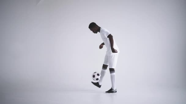 Slow motion: one african man soccer player white jersey juggling in silhouette on white background. One black Brazilian soccer football player man silhouette — Stock Video