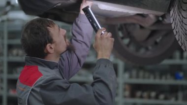 Ustabaşı bir arabanın egzoz sistemini kontrol eder.