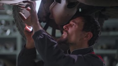 Ustabaşı bir arabanın egzoz sistemini kontrol eder.