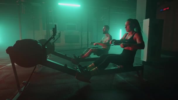 Movimiento lento: Hombre y mujer entrenando en una máquina de remo en gimnasio — Vídeos de Stock