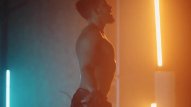 Tişörtsüz, çıplak gövdeli kaslı bir adam ağır çekimde ipe atlıyor. Bir dövüşçü ipin üzerinden atlar.