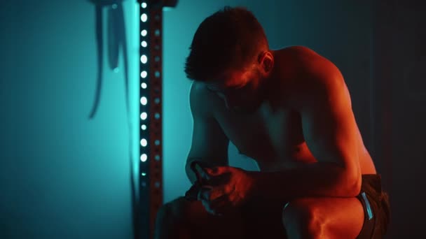 Unavený muž po cvičení sedí na čince a odpočívá v tělocvičně v modro-oranžových barvách ve zpomaleném filmu — Stock video